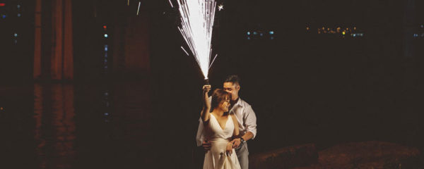 Photo de deux mariés. La mariée tient un feu d'artifice dans sa main droite.