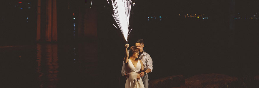 Photo de deux mariés. La mariée tient un feu d'artifice dans sa main droite.