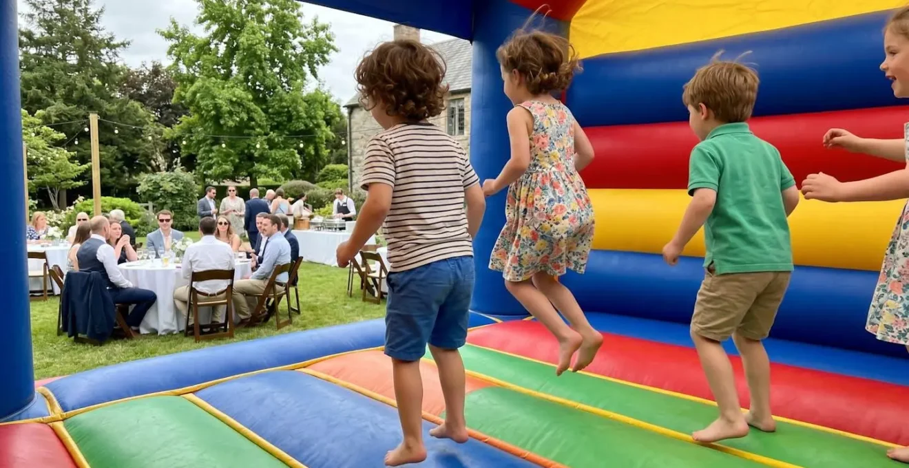 Plusieurs enfants vus de dos en train de sauter sur un château gonflable coloré, avec des adultes flous en arrière-plan discutant tranquillement